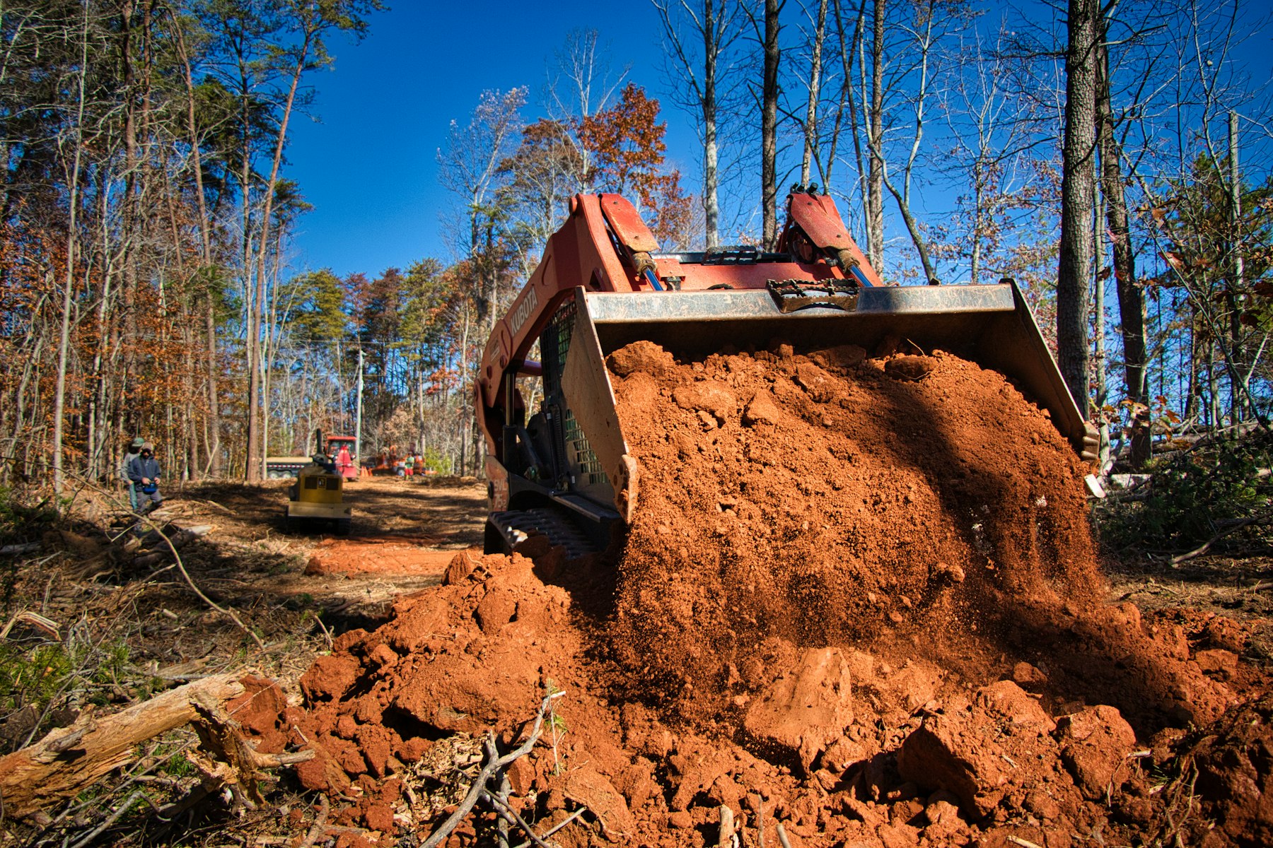 Heavy equipment moving dirt on a wooded rural property.